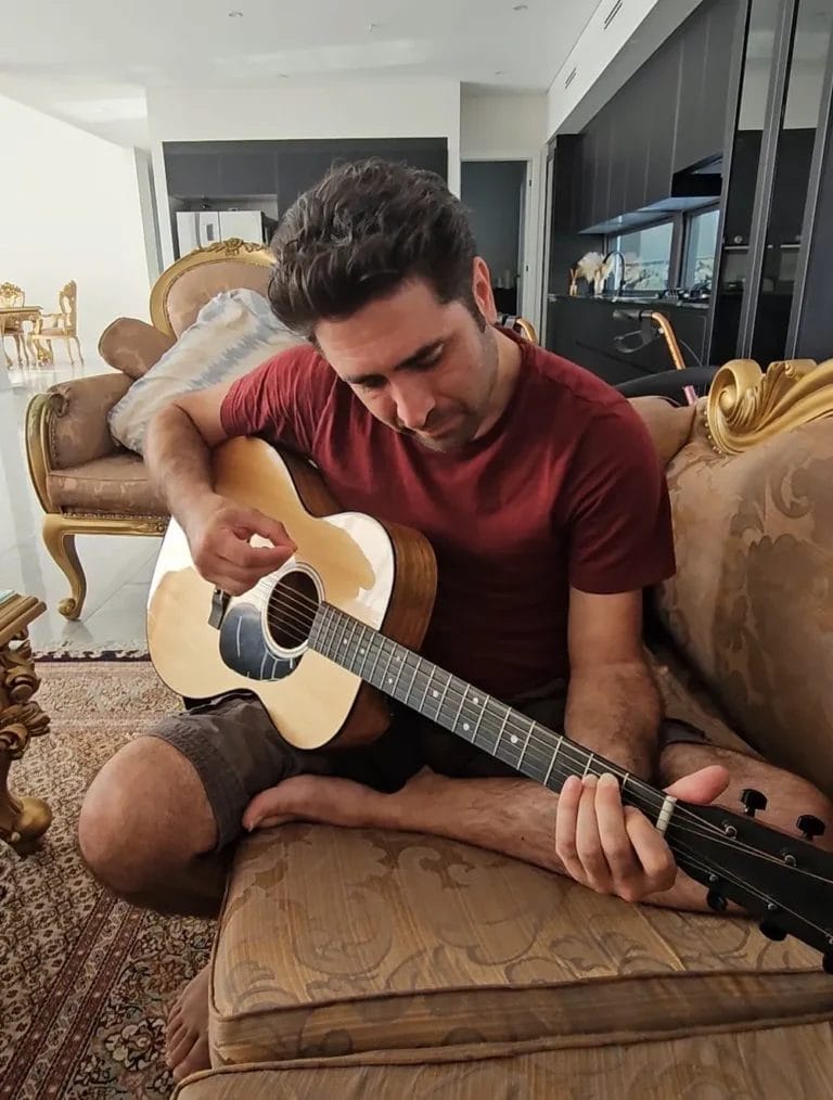 A person’s hands carefully learning to play a chord on an acoustic guitar during an NDIS capacity building program.
