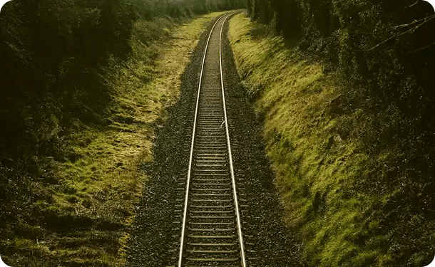A high-angle view of straight railway tracks stretching through a lush green landscape, symbolizing the clear, structured path and long-term support Jango Community Services provides to participants navigating the NDIS.