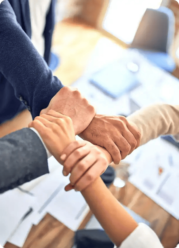 A close-up, high-angle view of four people interlocking their hands in a circle over a boardroom table, symbolizing the strength, unity, and collaborative spirit of the Jango Care Services team.