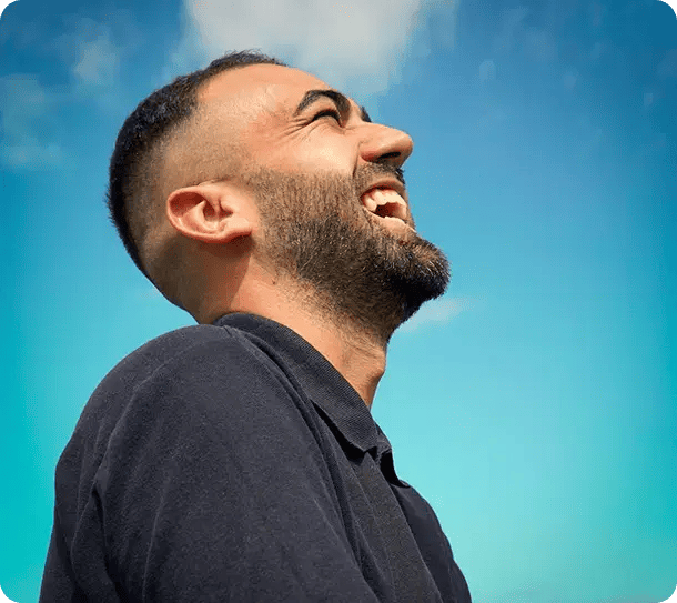 A close-up profile of a man laughing joyfully against a clear blue sky, capturing the ultimate goal of Jango’s NDIS support services: helping participants achieve a life of happiness, independence, and mental well-being.