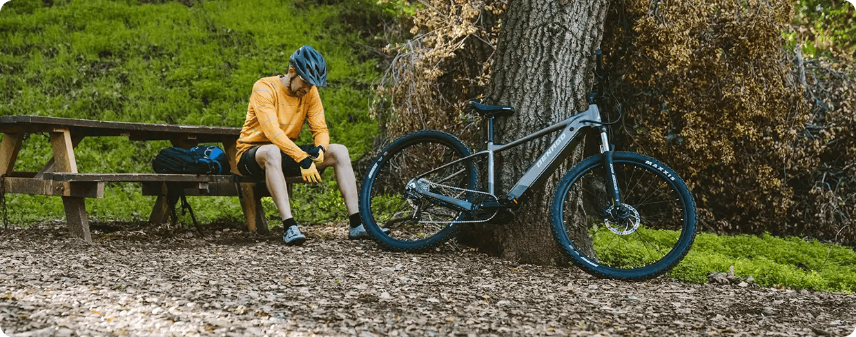 A man in cycling gear sitting on a park bench next to his electric bicycle, representing Jango’s NDIS programs that support physical health, community access, and independent lifestyle goals.