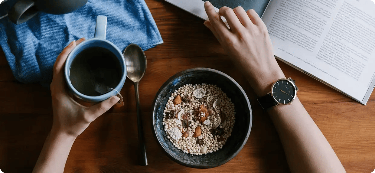 A top-down view of a person eating a healthy bowl of cereal and grains while reading a nutrition magazine next to a cup of tea, representing Jango’s 12-week program for personalized meal planning and wellness routines.