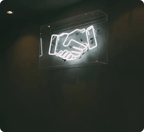 A glowing neon sign of a handshake on a dark wall, symbolizing the strong partnerships and professional coordination Jango Community Services builds with every participant.