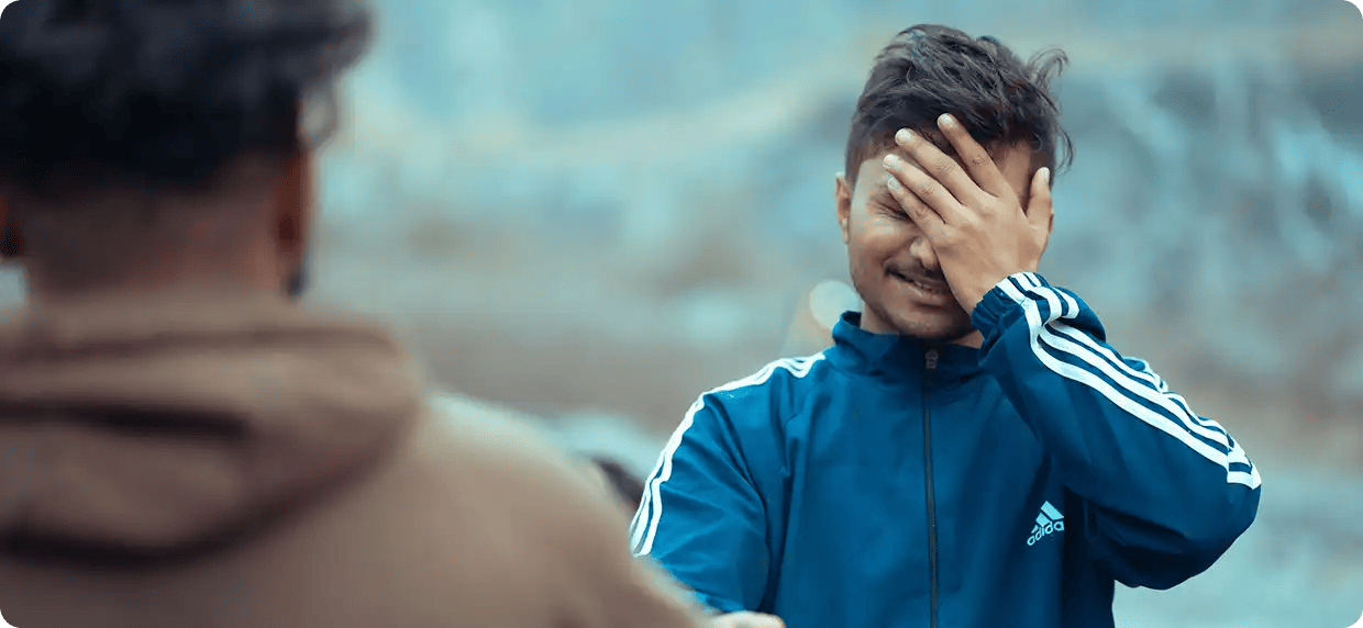A young man in a blue tracksuit covering his face with his hand in a moment of frustration while being supported by another person, representing Jango’s person-centred approach to understanding and managing challenging behaviours with dignity and empathy.