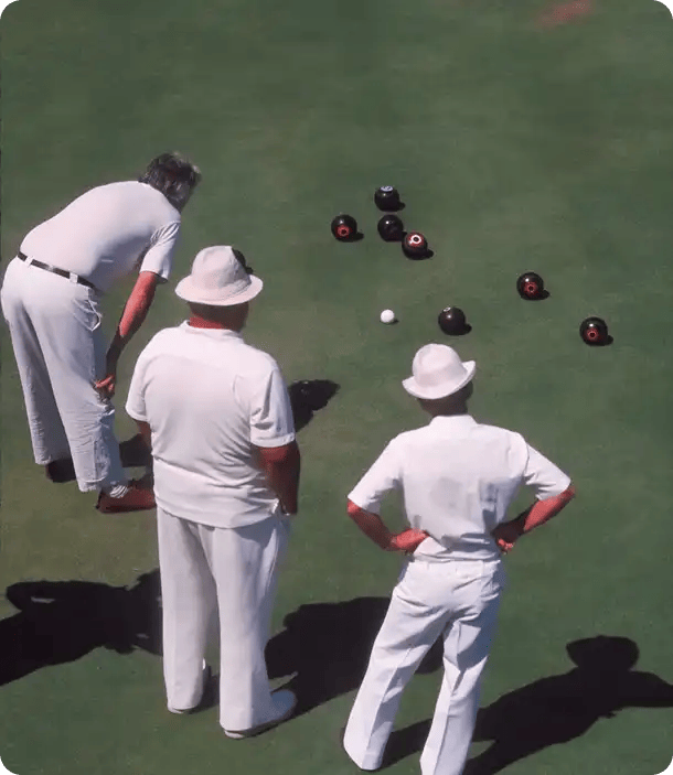 Three men in white sporting attire playing a game of lawn bowls on a green, representing the social inclusion and community participation goals Jango helps NDIS participants achieve through expert support coordination.