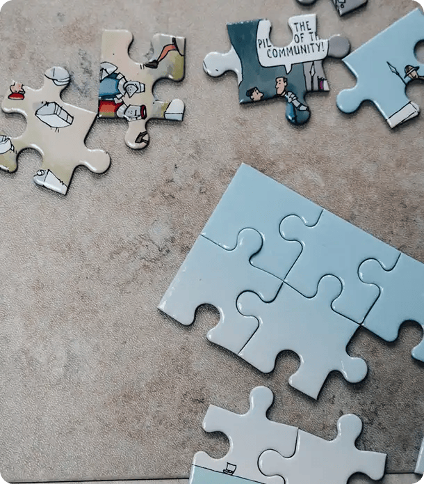 Scattered jigsaw puzzle pieces on a table, with one piece featuring a cartoon bubble that says "The Pillars of the Community," representing Jango’s mission to help participants find their place and build strong social connections.