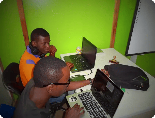 Two young men working on laptops in a vibrant green workspace, representing Jango’s capacity-building programs that focus on technology skills and career development.