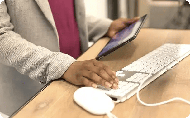 A close-up of a person simultaneously using a tablet and a computer keyboard at a wooden desk, symbolizing Jango’s efficient use of technology to manage NDIS plans and provide remote support for participants in the Toowoomba region.