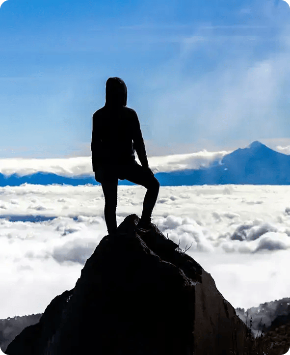 A silhouette of a person standing triumphantly on a mountain peak above a sea of clouds, symbolizing the personal growth and peak independence Jango helps NDIS participants achieve through local support in Brisbane.