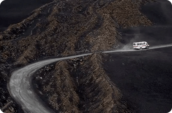 A white van driving along a winding, dusty road through a dark, rugged mountain landscape, symbolizing Jango’s commitment to supporting NDIS participants through complex challenges and providing reliable transport to essential services.