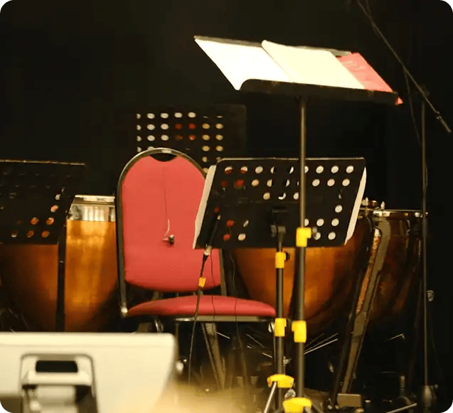 A set of music stands, a red chair, and orchestral percussion instruments (tympani) on a stage, representing the diverse range of musical genres and professional workshop environments provided by the Jango Jams program.