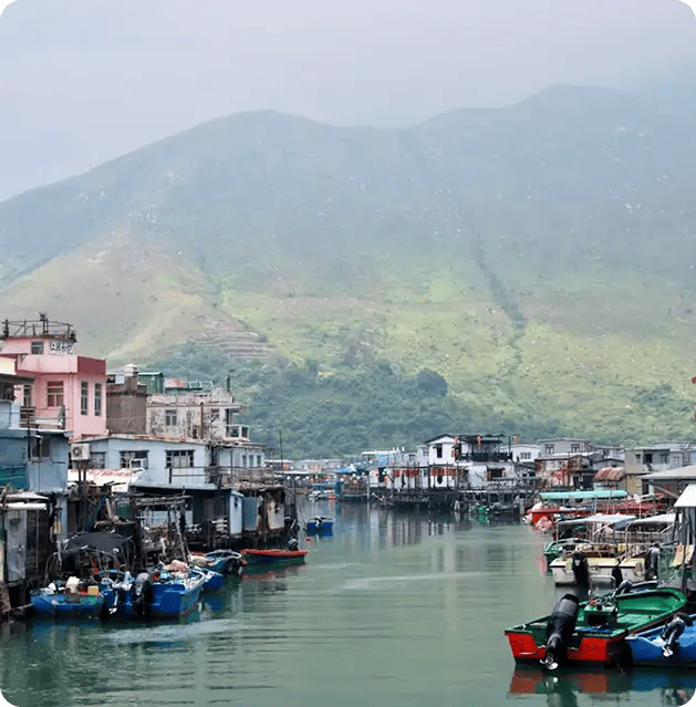 A tranquil coastal village with colorful boats on calm water against a backdrop of mist-covered mountains, representing the peaceful environments and community inclusion fostered through Jango's recovery programs.