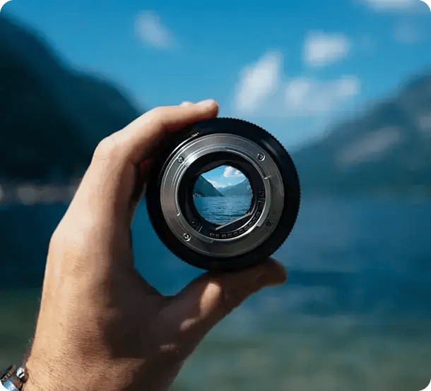 A person holds a camera lens up to a beautiful coastal landscape, focusing the view of the water and mountains, representing Jango’s ability to help Gold Coast participants find clarity and focus in their NDIS goals.