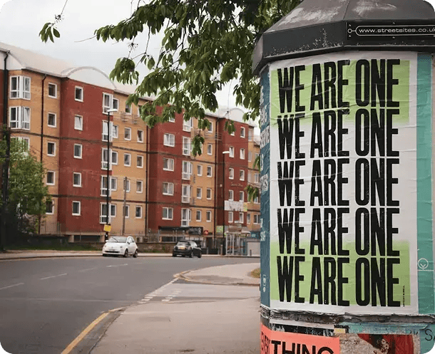 A street scene featuring a pillar with a large poster repeating the phrase "WE ARE ONE," with residential buildings in the background, representing Jango’s commitment to social inclusion and community connection for NDIS participants.