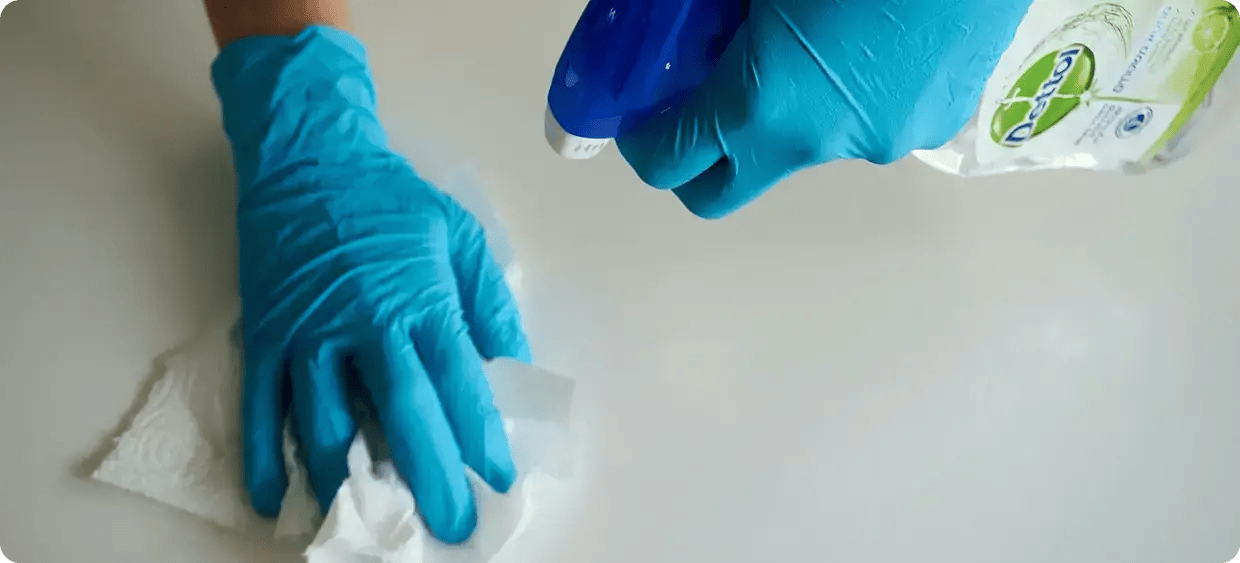 A person wearing blue protective gloves using a disinfectant spray and a white cloth to clean a surface, representing professional NDIS domestic assistance and cleaning services provided by JANGO Community Services.