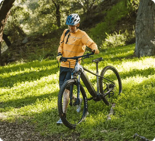 A man in a helmet and yellow shirt standing with his electric mountain bike on a grassy trail, representing Jango’s NDIS support for active community participation and outdoor hobbies.