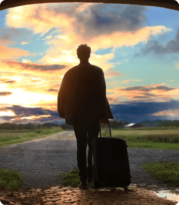 A silhouette of a man pulling a suitcase as he walks down a rural road toward a vibrant sunset, representing the "Road Ahead" phase of Jango’s Pathways to Potential program where participants transition into their new vocational or personal journeys.