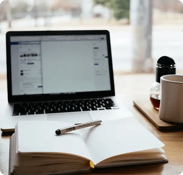 A clean, sunlit workspace featuring an open laptop, a notebook with a pen, and a coffee mug, representing the structured goal-setting and administrative support Jango provides for NDIS plan management and capacity building.