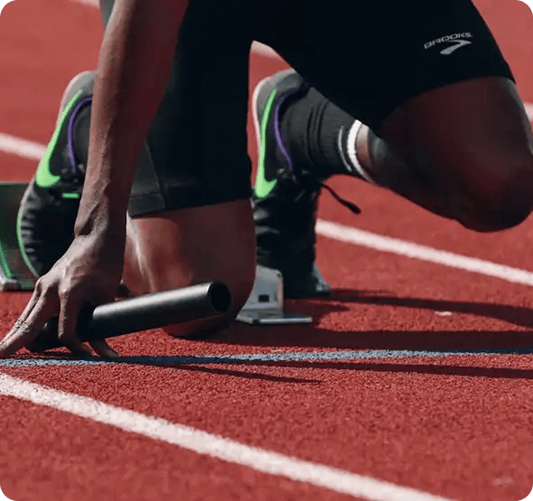 A close-up of a sprinter at the starting blocks holding a relay baton, symbolizing Jango’s NDIS support for participants pursuing high-level athletic goals and community sports participation.