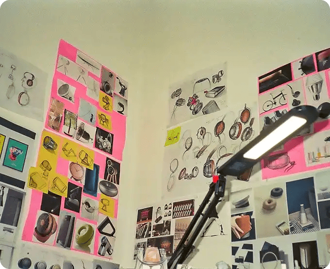 A wall covered in vibrant pink and yellow post-it notes, sketches of headphones, and design concepts under a desk lamp, representing the creative brainstorming and goal-setting workshops used in Jango's NDIS programs to help participants map out their interests and future aspirations.